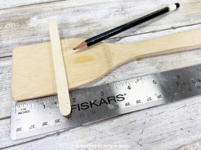 Wooden spoon with craft stick and ruler showing how to measure and mark the pencil line for Uncle Sam's hat.