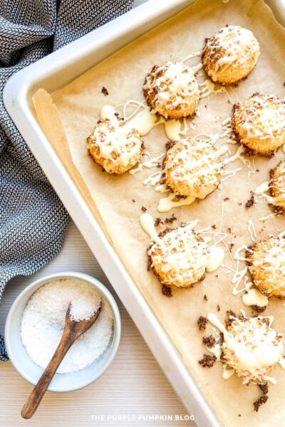 Baked coconut macaroons on parchment, generously drizzled with melted white chocolate and ready to chill.