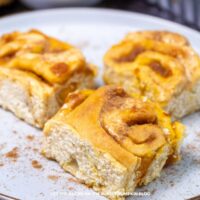 Soft cinnamon roll cake squares with a swirled cinnamon sugar filling on a white plate. Treat yourself to Fluffy Pumpkin Cinnamon Rolls made from scratch! These golden rolls are filled with pumpkin, cinnamon, and nutmeg, then drizzled with a pumpkin cream cheese glaze. Ideal for brunch, Thanksgiving, or any fall gathering. Head to The Purple Pumpkin Blog for the complete recipe!