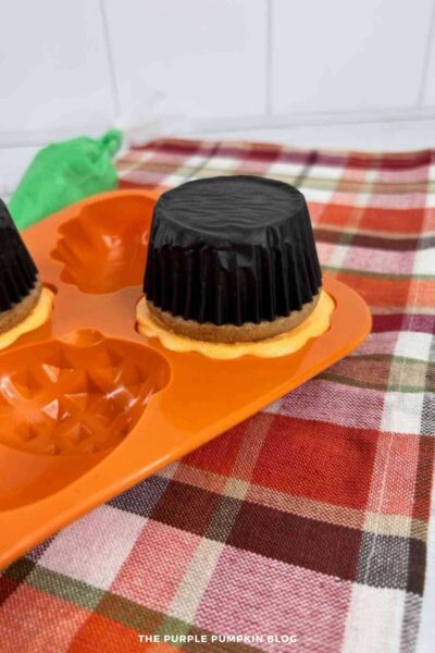 A cupcake inverted and pressed into a filled silicone mold cavity to attach the pumpkin-shaped frosting.