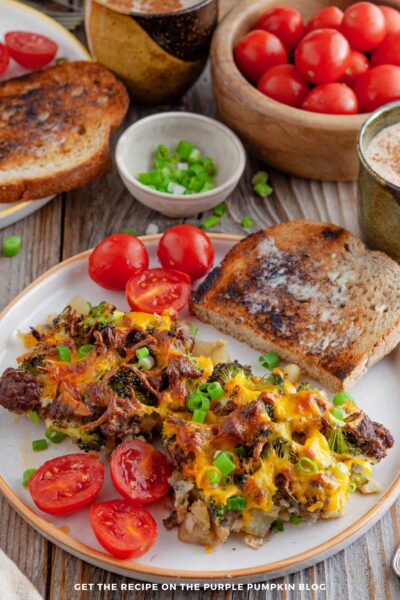 Plate of potato and sausage breakfast casserole topped with melted cheddar cheese and green onions, served with toast and tomatoes.