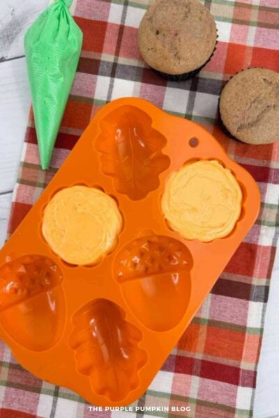 Orange cream cheese frosting piped into a silicone pumpkin mold cavity, smoothed level with a spatula.