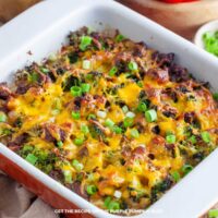 Sausage and potato breakfast casserole baked in a white dish, topped with melted cheddar and chopped green onions.