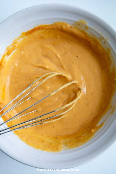 Creamy pumpkin cinnamon roll frosting being mixed with a whisk in a white bowl.