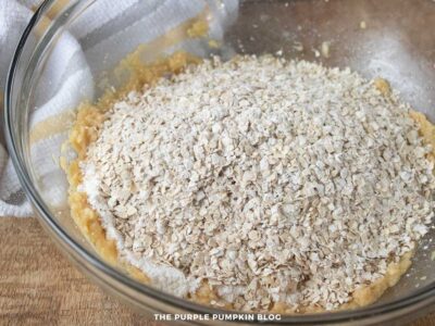 Bowl of creamed butter mixture with oats and flour mixture added on top, ready to be mixed.