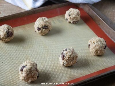 Unbaked oatmeal raisin cookie dough balls placed on a silicone baking mat on a baking sheet.