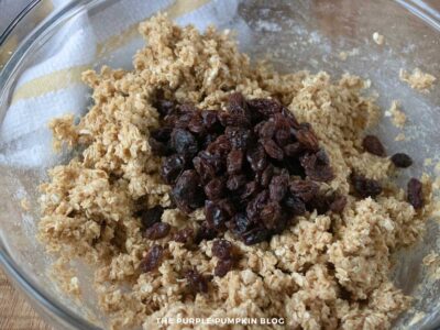 Mixing bowl with cookie dough and a pile of raisins on top before being stirred in.