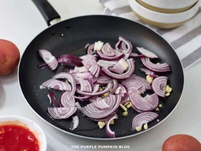 Sliced red onions and chopped garlic sautéing in a skillet with oil.