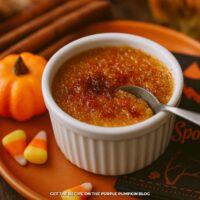 Pumpkin pie crème brûlée in ramekin with a spoon inserted. Surrounded by Halloween decor.