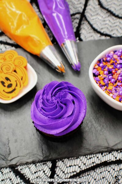 Vibrant purple Halloween cupcake with colorful sprinkles and themed decorations.