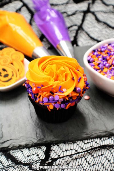Sprinkle-topped Halloween cupcake with orange frosting and colorful sprinkles.