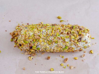 Pistachio and walnut coated cheese log resting on parchment paper.