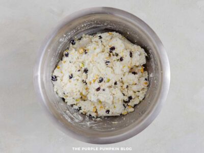 Cream cheese mixture with chopped pistachios and dried blackcurrants in a metal mixing bowl.