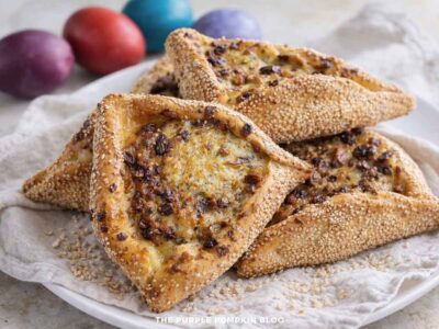 A plate of Flaounes - Cypriot Easter Cheese Bread on a plate with a cloth and some dyed eggs in the background.