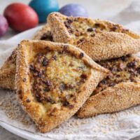 A plate of Flaounes - Cypriot Easter Cheese Bread on a plate with a cloth and some dyed eggs in the background.