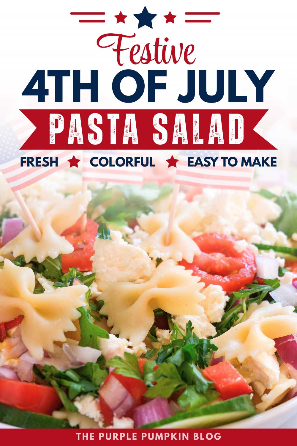 White bowl filled with bowtie pasta salad topped with cherry tomatoes, cucumber slices, red onion, parsley, crumbled feta cheese, and small American flag picks on a light marble surface.