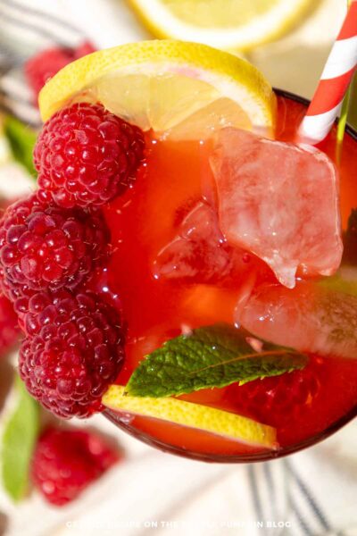 A glass of Raspberry Mojito Mocktail garnished with fresh raspberries, lemon slices, and fresh mint