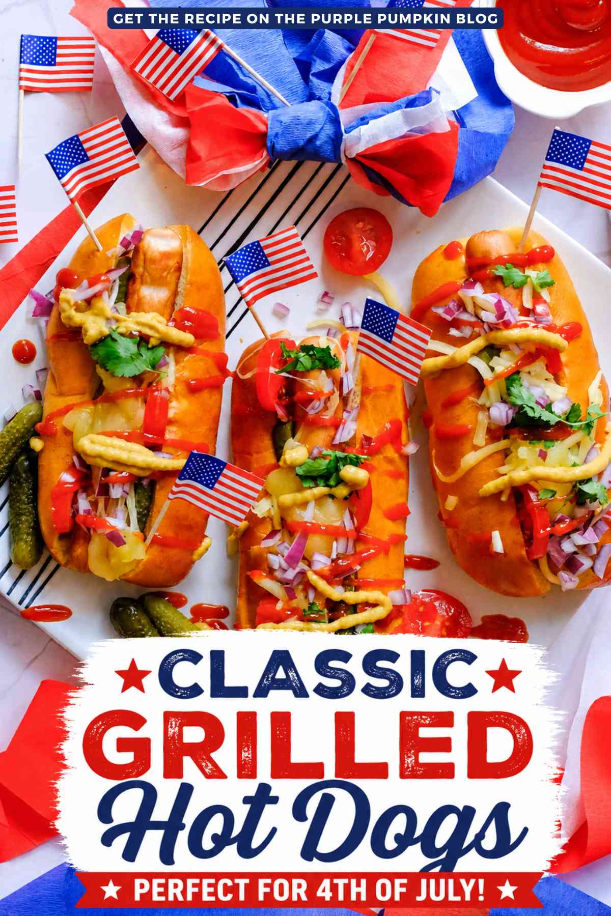 Three loaded grilled hot dogs topped with cheese, pickles, diced red onion, ketchup, and mustard on a white platter with American flags and patriotic decorations. Text overlay says: "Classic Grilled Hot Dogs Perfect for 4th of July!"