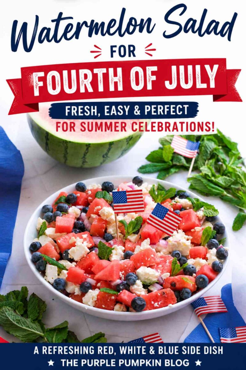 A white serving bowl filled with a watermelon salad made with juicy watermelon cubes, crumbled feta cheese, fresh blueberries, diced red onion, and mint leaves. The salad is garnished with small American flags and photographed with half a watermelon and fresh mint in the background.
