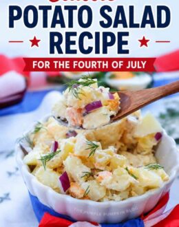 A white scalloped bowl filled with creamy potato salad made with chunks of potato, chopped hard-boiled egg, diced red onion, and fresh dill. The bowl is wrapped with red, white, and blue tissue paper. Text overlay says "Classic Potato Salad Recipe for the Fourth of July. Creamy, Easy, BBQ Favorite"