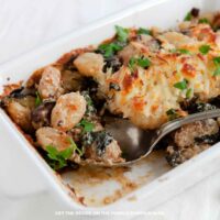 Baked Gnocchi with Italian Sausage: Baked gnocchi with Italian sausage, mushrooms, spinach, and melted cheese in a white casserole dish, garnished with fresh parsley.