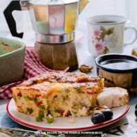 Goat Cheese Breakfast Casserole: Slice of baked goat cheese breakfast casserole with vegetables, served on a plate with bread, blueberries, and coffee.