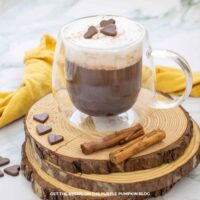 A glass mug filled with pumpkin spice hot chocolate topped with chocolate hearts
