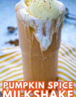 A tall glass of pumpkin spice milkshake topped with whipped cream and a scoop of vanilla ice cream, served on a striped cloth.