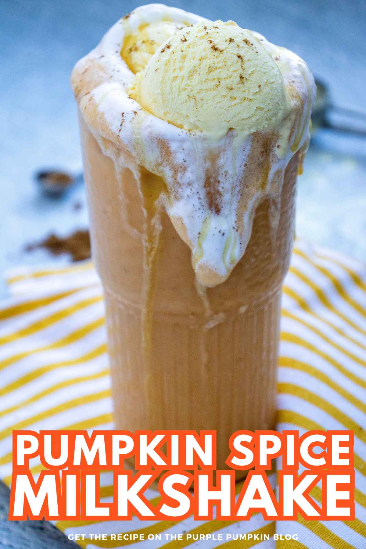 A tall glass of pumpkin spice milkshake topped with whipped cream and a scoop of vanilla ice cream, served on a striped cloth.